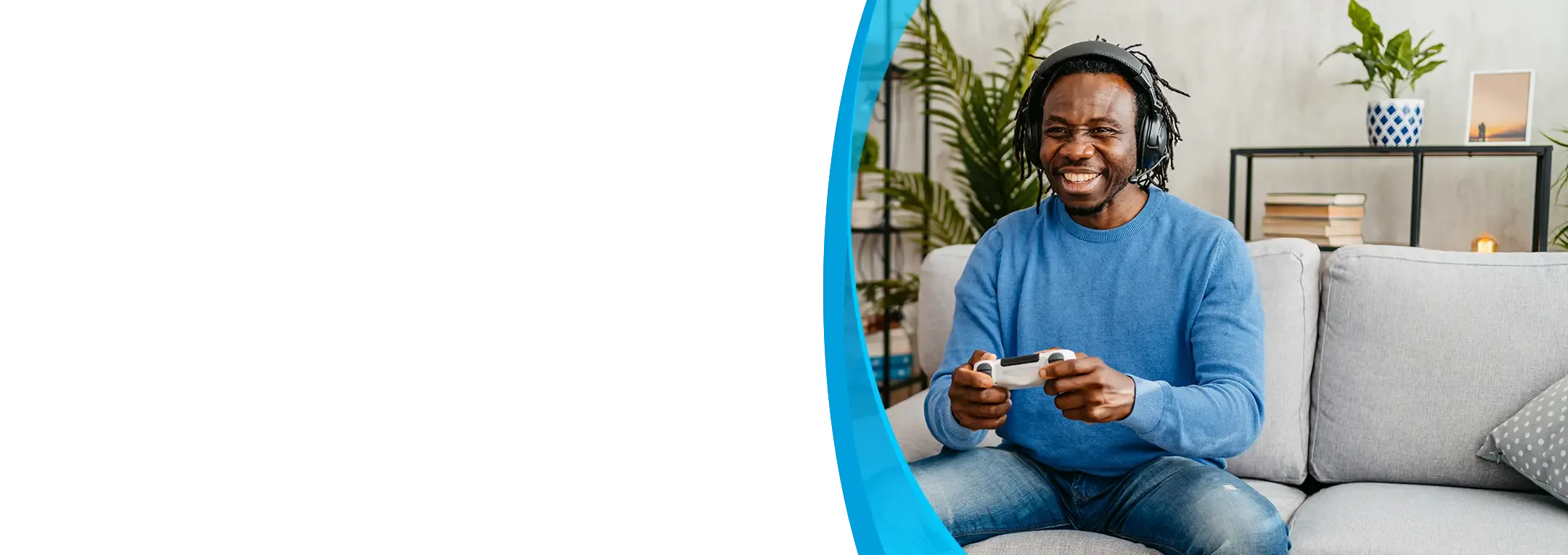A smiling man wearing headphones plays a video game with a controller on his couch.